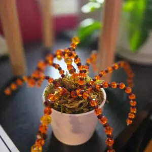 A beaded spider crafted with orange and black beads on a white pot.