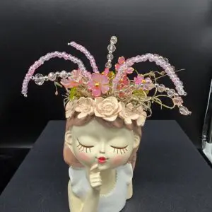 Ceramic planter shaped like a serene face with pink flowers and greenery.