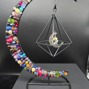 A colorful crescent structure holding a geometric cage with a moon and figure inside.