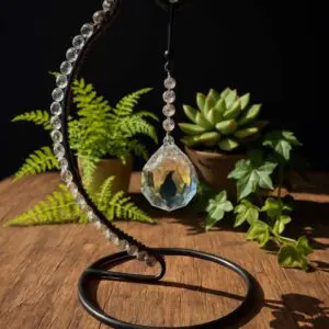 Crystal pendant hanging on a metal spiral stand with plants in the background.