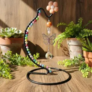 Colorful beaded bird toy hanging on a curved stand surrounded by plants.