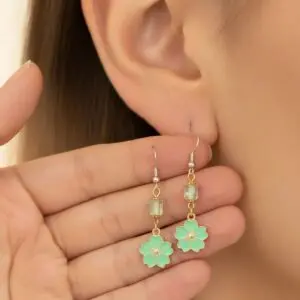 Close-up of hand holding green floral earrings near ear.