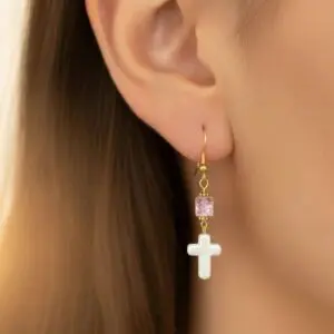 Close-up of a gold earring with a white cross and purple bead.